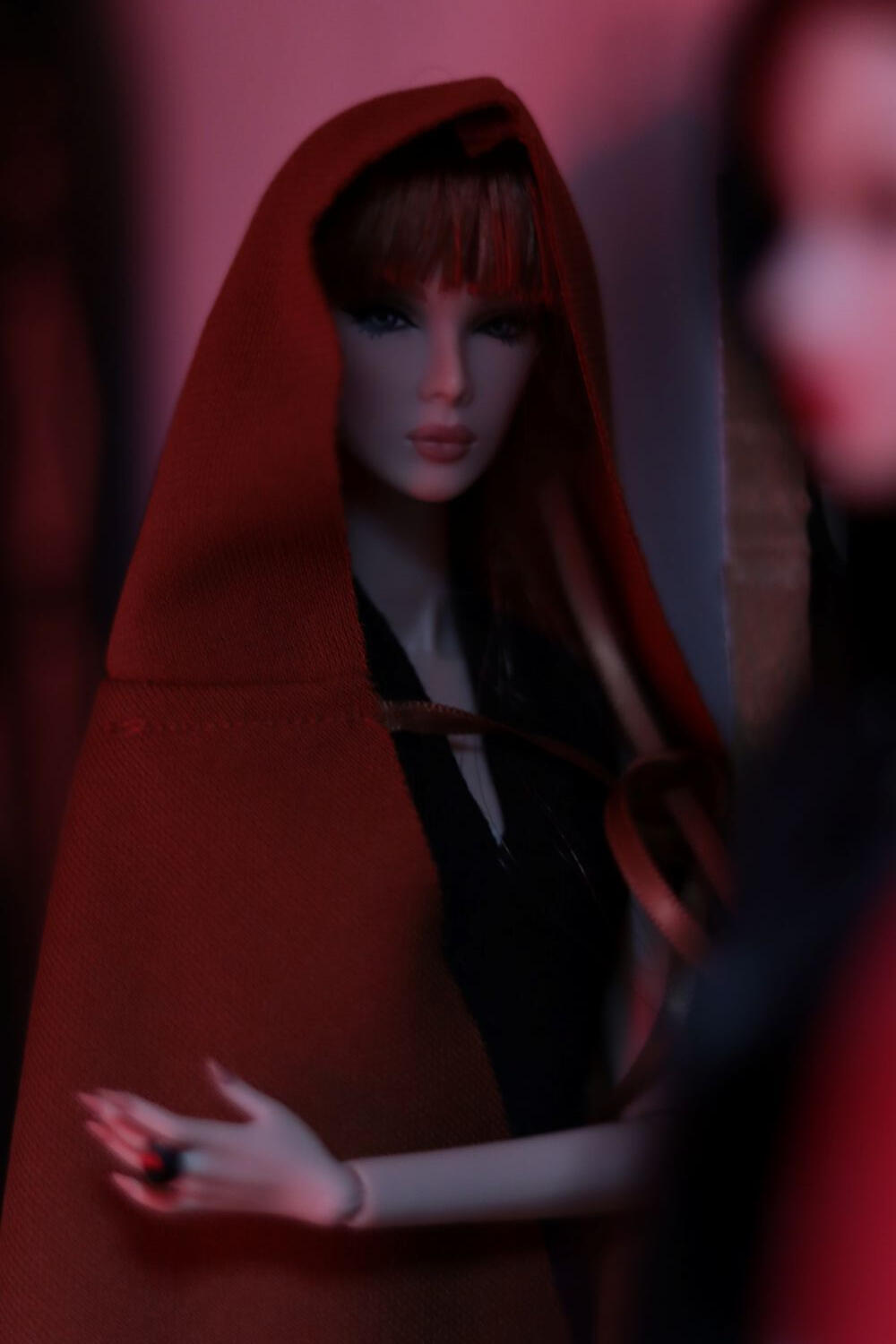 Artistic doll photograph showing a Eden Blair doll partially wrapped in a red cloak under dramatic, low light